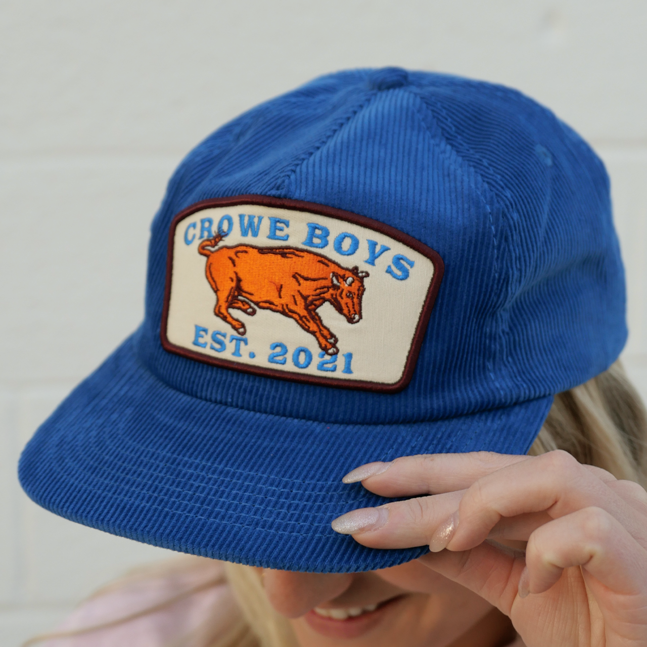 model wearing a blue corduroy flat bill hat with a bull patch design